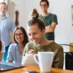A group of friends enjoying a moment together indoors, smiling and watching a video on a laptop.