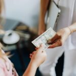 Close-up of a transaction involving a US dollar bill exchanged indoors between two individuals.